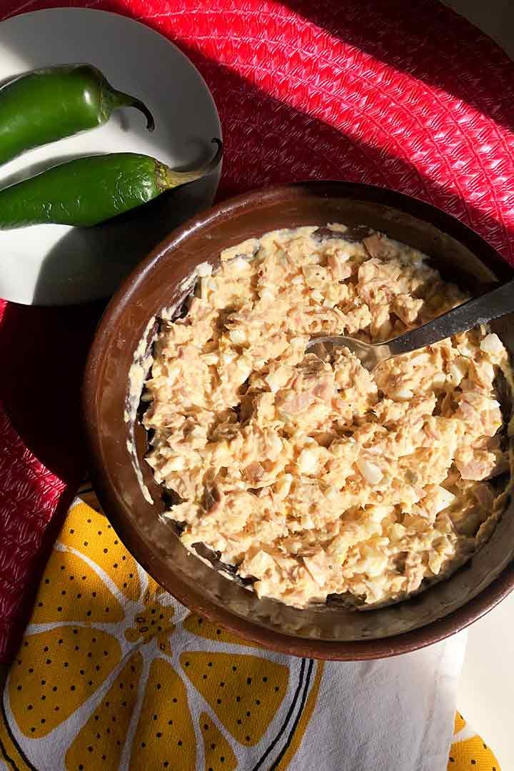 Tuna Salad plated in bowl with whole fresh jalapenos above it on mexican pink colored surface.