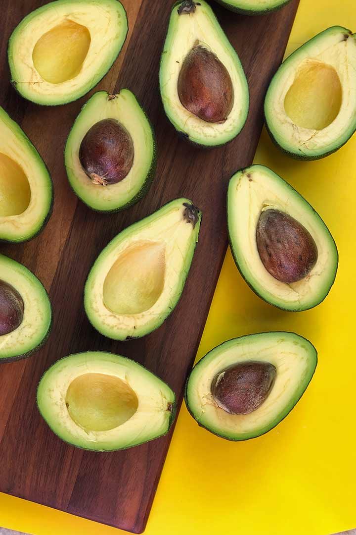 How to Freeze Avocados post. ripe avocados, cut side up on dark wood and yellow chopping board.