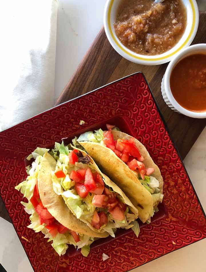 tacos on a red square plate with salsas beside it.