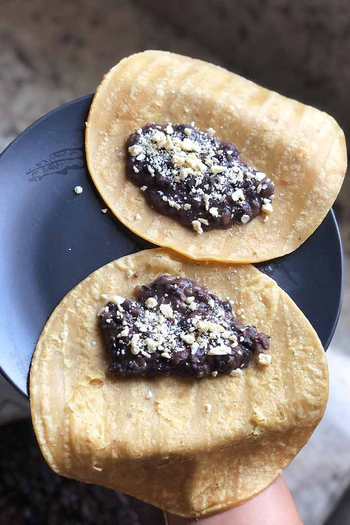 two-refried-black-bean-tacos-on-yellow-corn-tortilla-on-dark-plate.