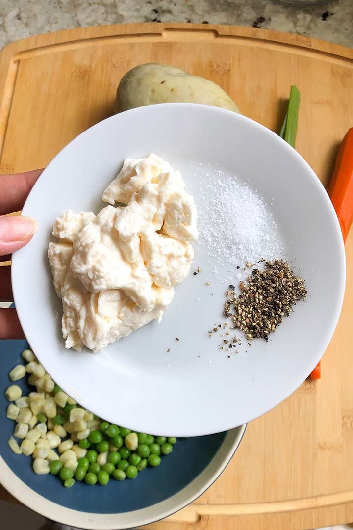 Hand holding white plate with mayonnaise, salt and pepper on it.