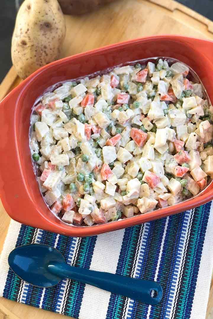 Russian Salad Ensalada Rusa in a large orange bowl on top of Mexican knit blue napkin pictured at an angle.