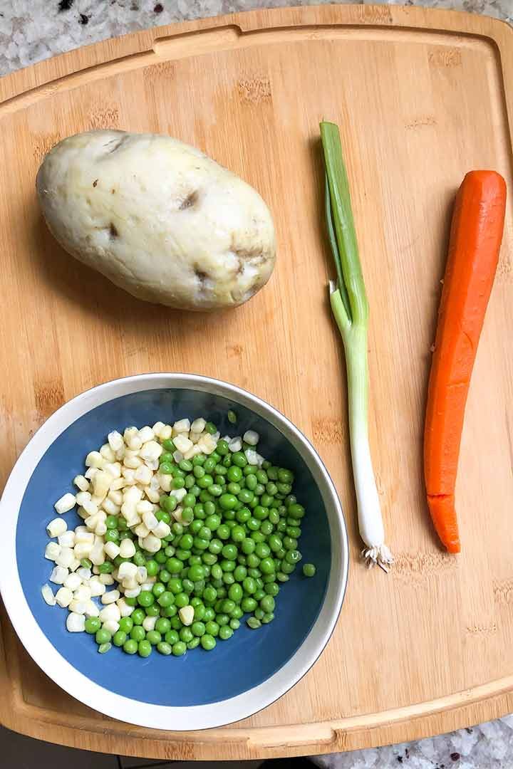 Cooked and frozen vegetable ingredients for recipe on a light wood cutting board.