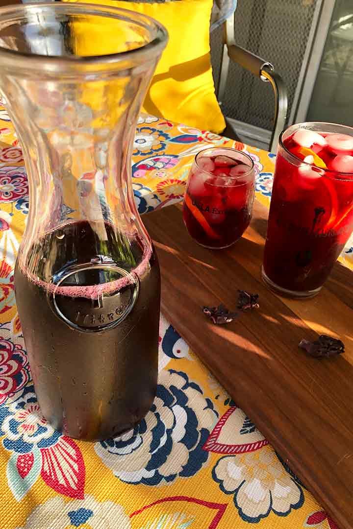 Glass Pitcher and cups of Agua de Jamaica for alfresco dining on a tablecloth.