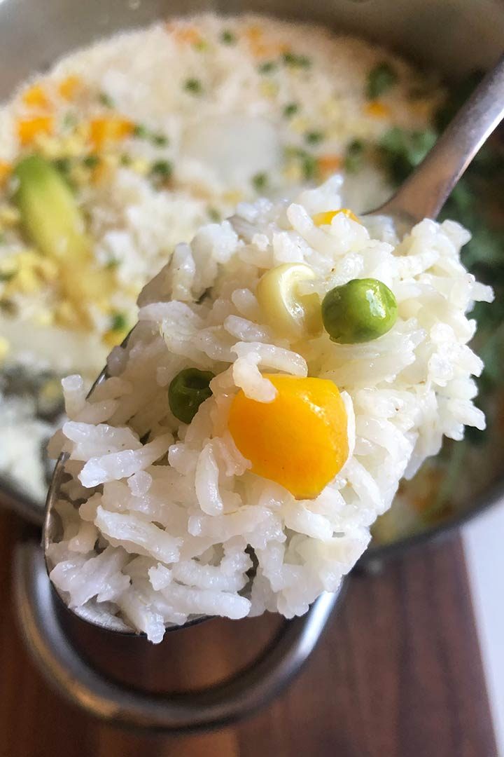 Close up of cooked Mexican White Rice on a spoon with pan of rice in background.