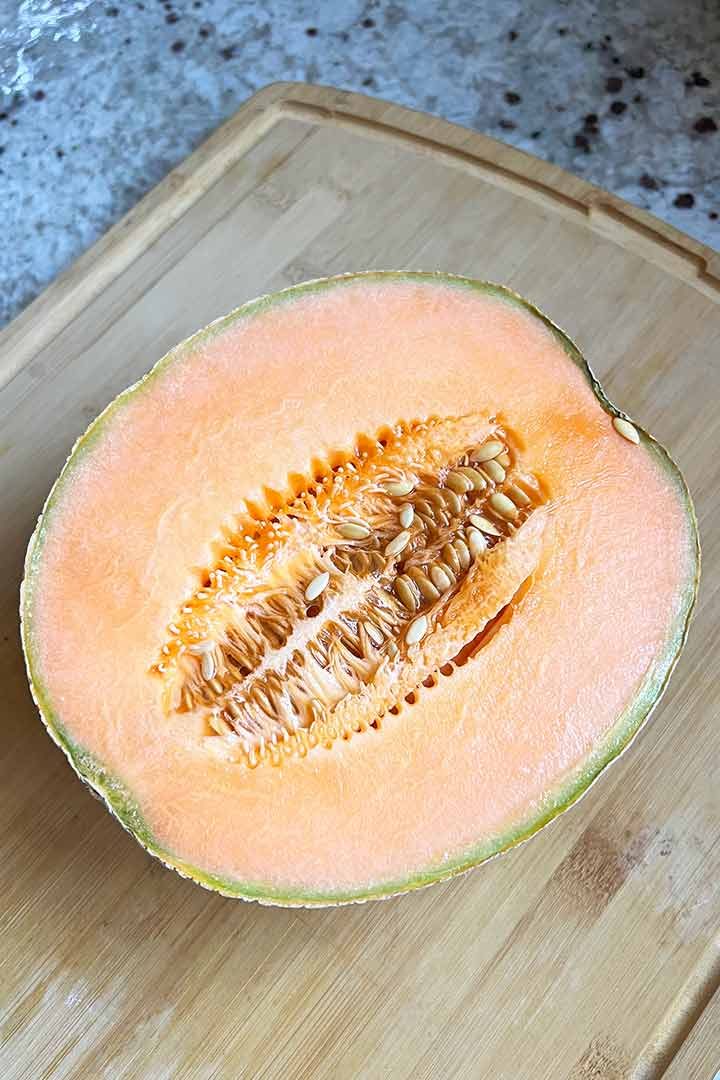 Half of a fresh Cantaloupe with Seeds on a wood surface with granite in background.