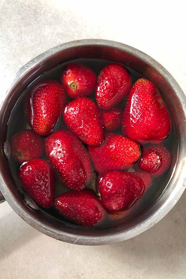 Washed strawberries covered in small pot on white surface.