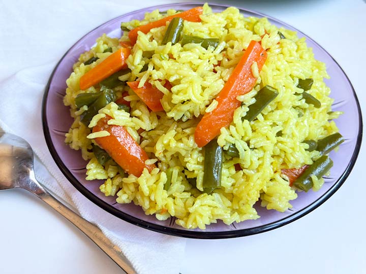 Plated Yellow Mexican Rice Recipe with vegetables on purple round glass plate.