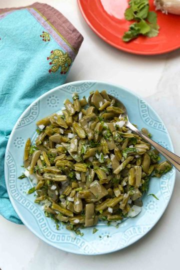 Best cooked Nopales recipe centered on plate with spoon, blue hand knit napkin aside it...