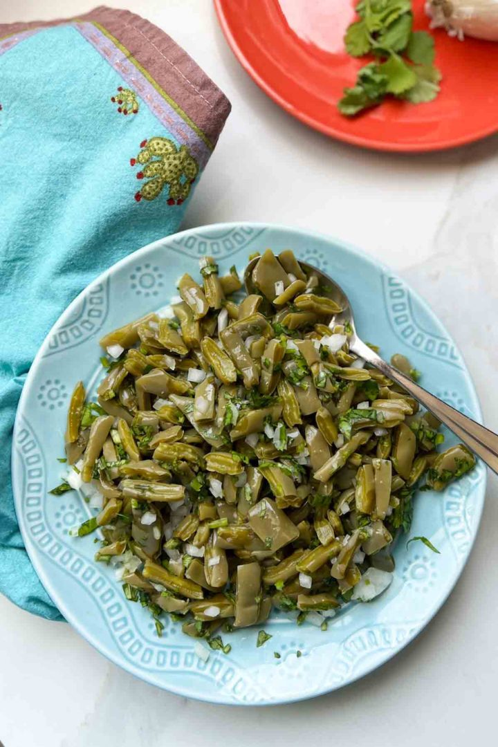 Cooked Nopal side salad centered on plate with spoon, blue hand knit napkin aside it.