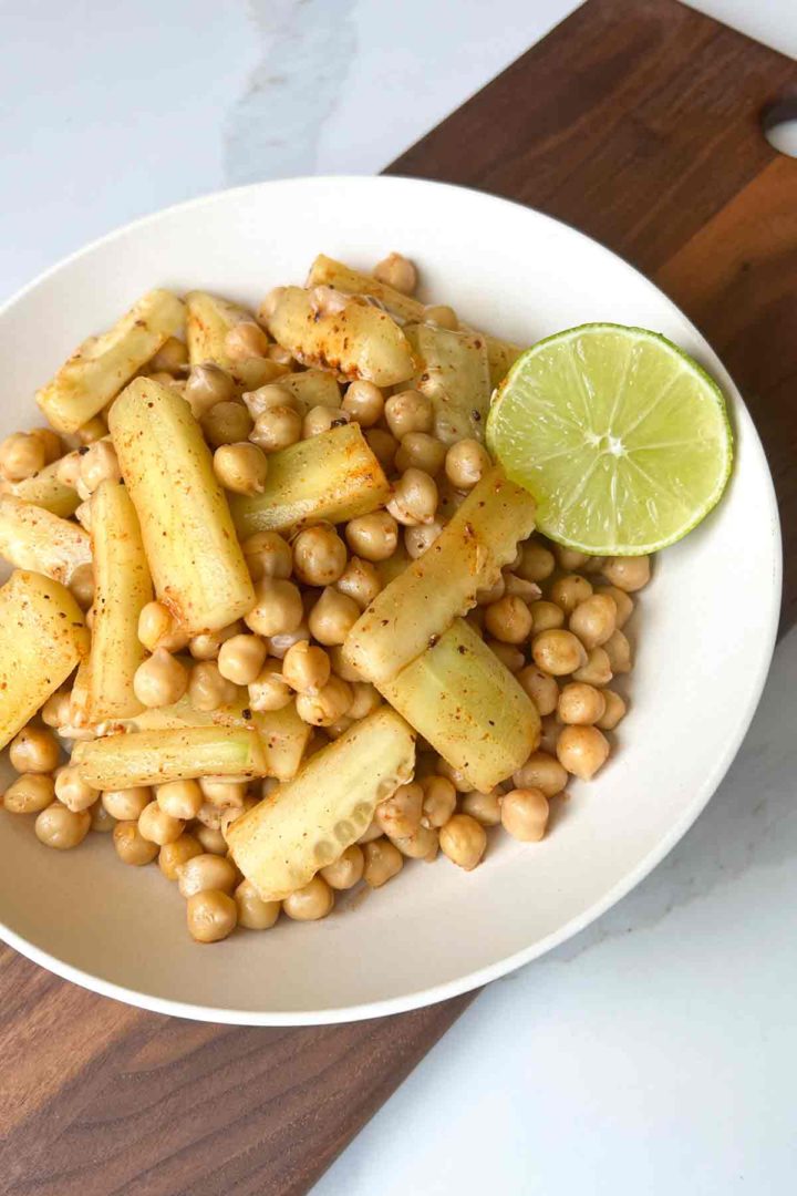 tender Garbanzo Bean Snack with cucumber in a round bowl with halved lime on brown wood and white surface.