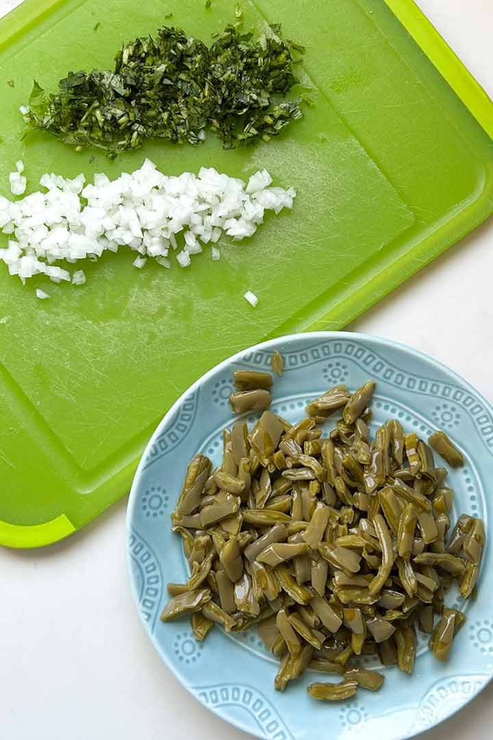 Nopales on a blue plate and diced onion and cilantro on limegreen cutting board.