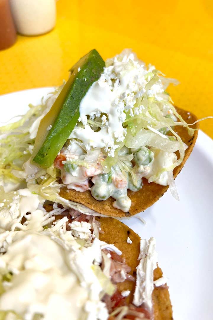 Tostadas with veggies slice of avocado on a plated on yellow surface.