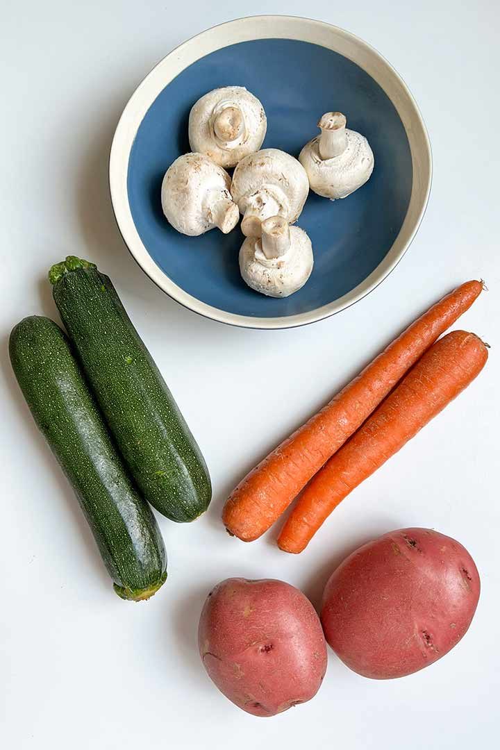 Ingredients, fresh mushroom, zucchini, red potatoes, and fresh carrots on white surface.