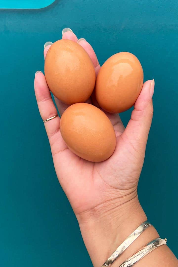 three fresh eggs in a hand, 1 of 2 top ingredients in recipe