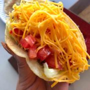 Erika's Hand holding a Shredded Beef Crunchy Taco with diced tomato and cheese shreds.