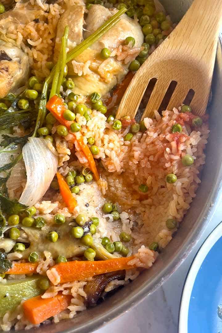 Final image, fresh cooked chicken and rice with green peas recipe in the pan with wood serving spoon.