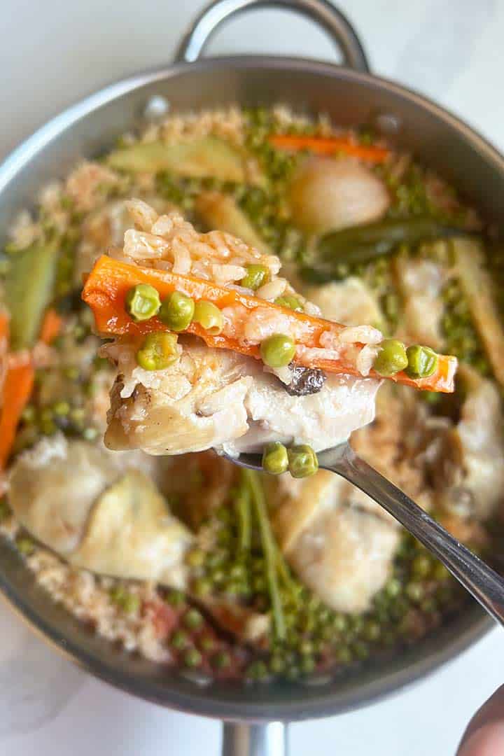 spoonful with chicken rice carrot and peas raised above large pan.