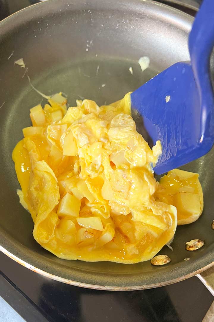 Potato and eggs cooking and gently turning with spatula.