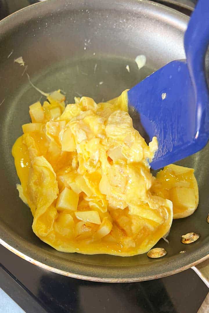 Potato and eggs cooking and gently turning with spatula.