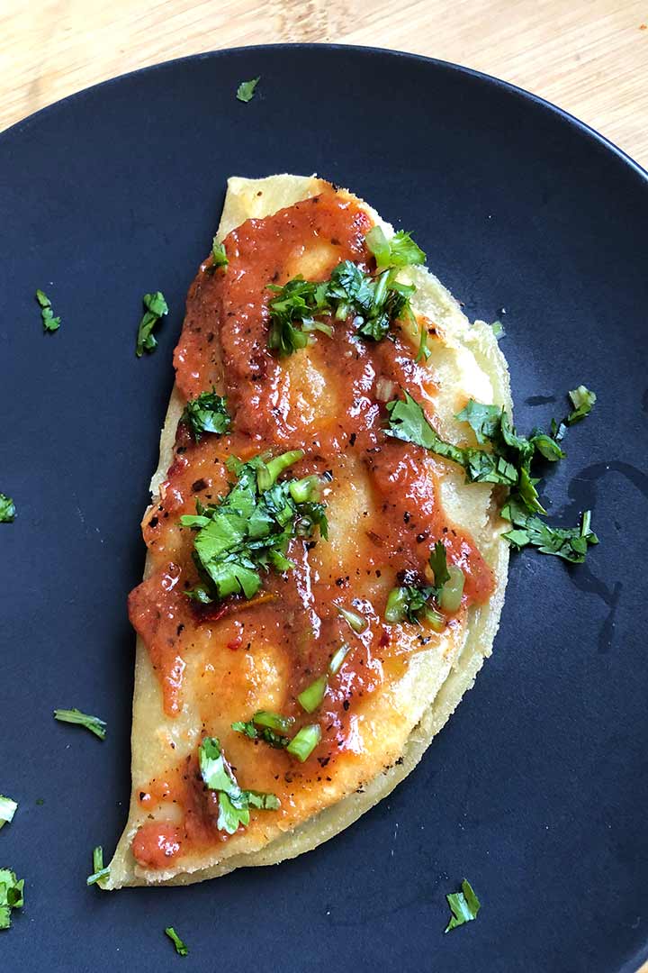 Potato Taco smothered in spicy red salsa and chopped cilantro on a dark ceramic plate.