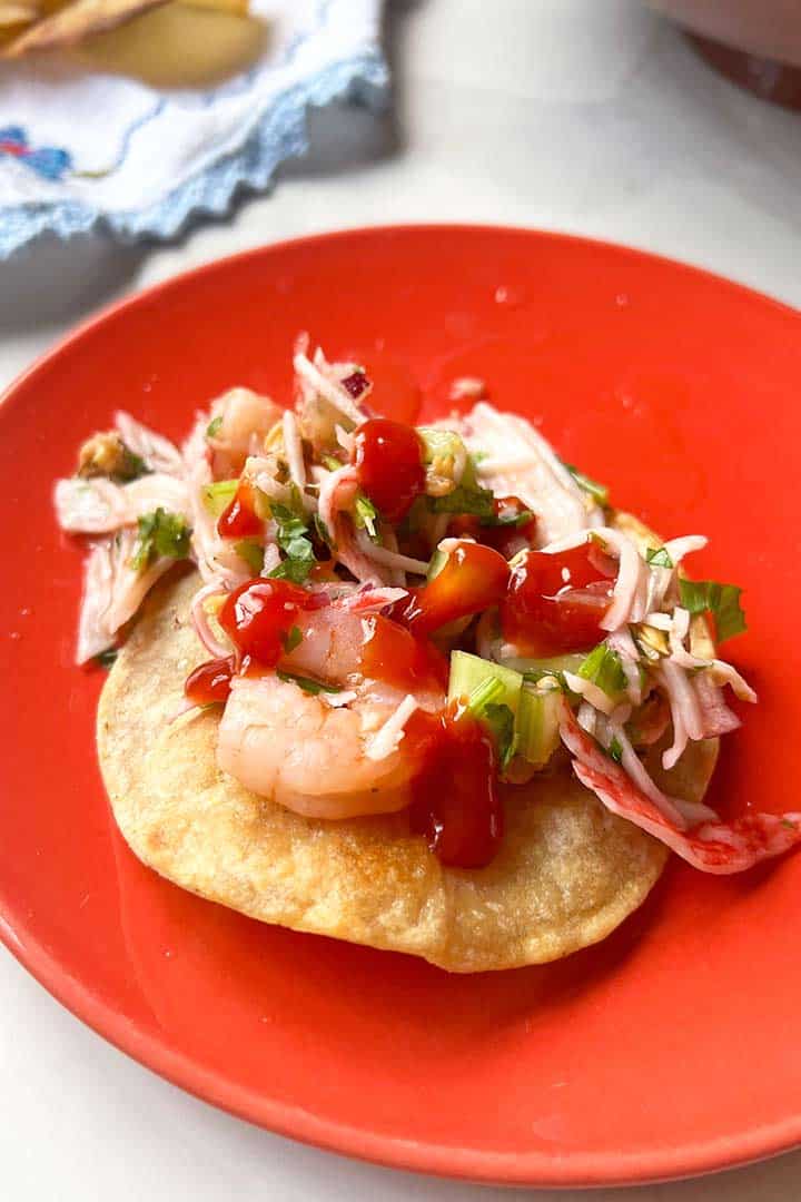 Seafood Ceviche Tostada with shrimp and Ketchup on a coral color plate.