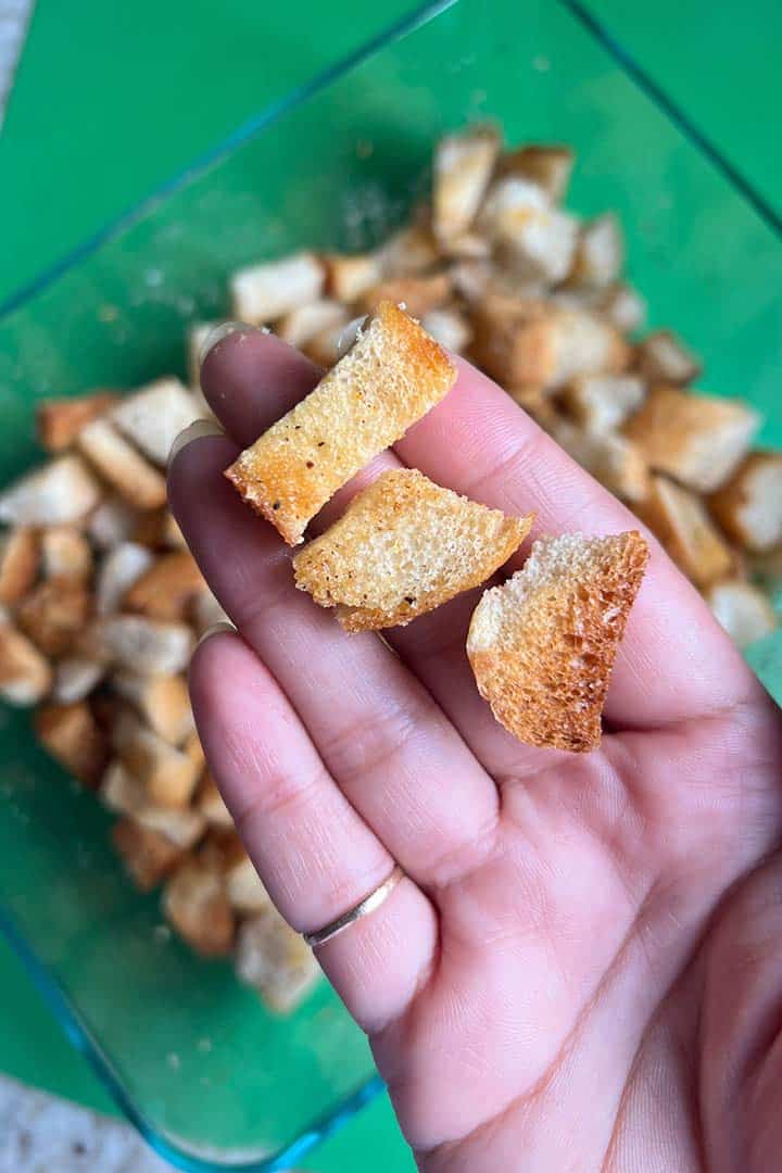 womans hand holding up three pieces of baked croutons for scale.