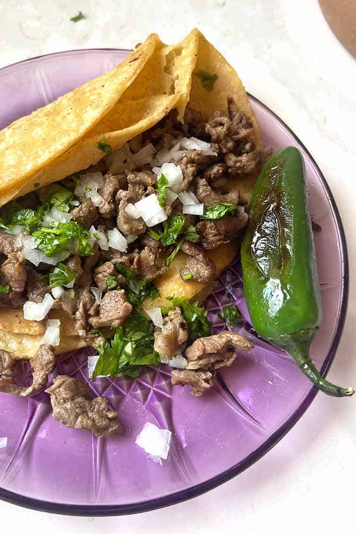 carne asada taco garnished with diced cilantro and onion on top and a Spicy Chile Toreado on the side.