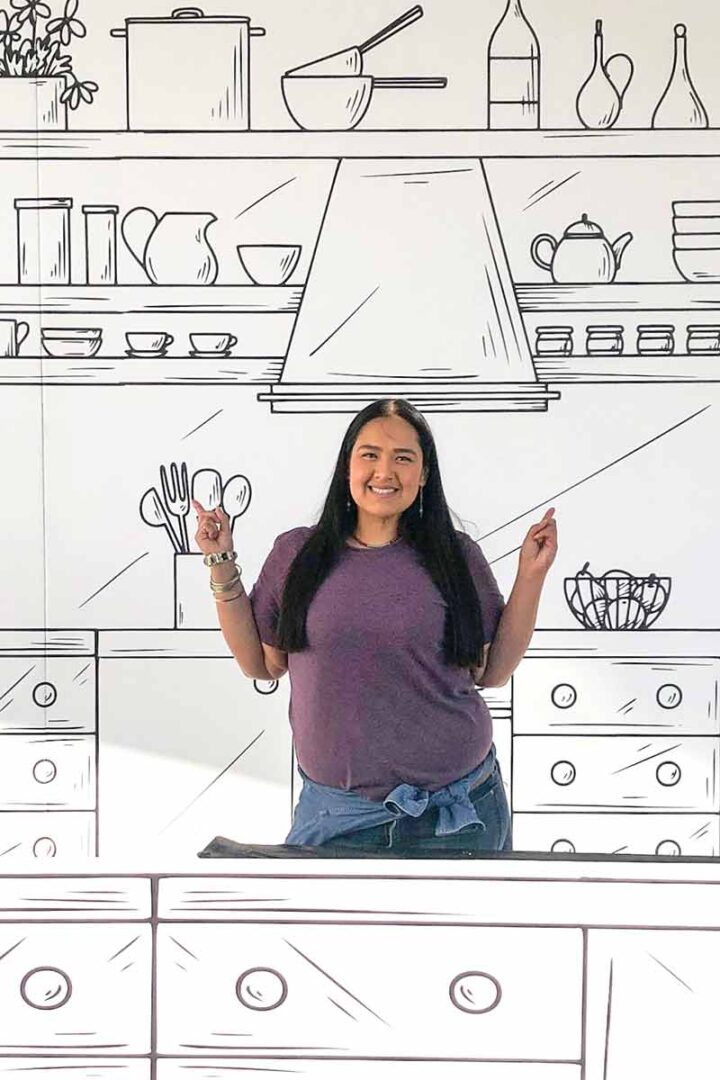 Proud LATINA Founder of LQC happily smiling with hands in air and index fingers symboling #1 Best, in an American Kitchen.