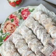 A platter of Mexican Wedding Cookies on floral plate with black coffee in a decorative mug above it.