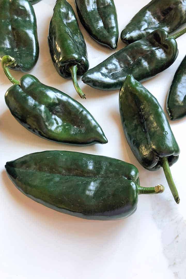 Ingredient to make recipe fresh poblano peppers on a white kitchen counter.