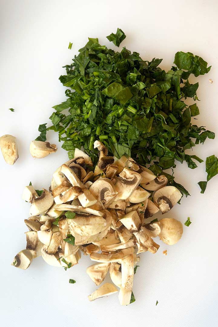 Chopped spinach and mushrooms on kitchen surface.