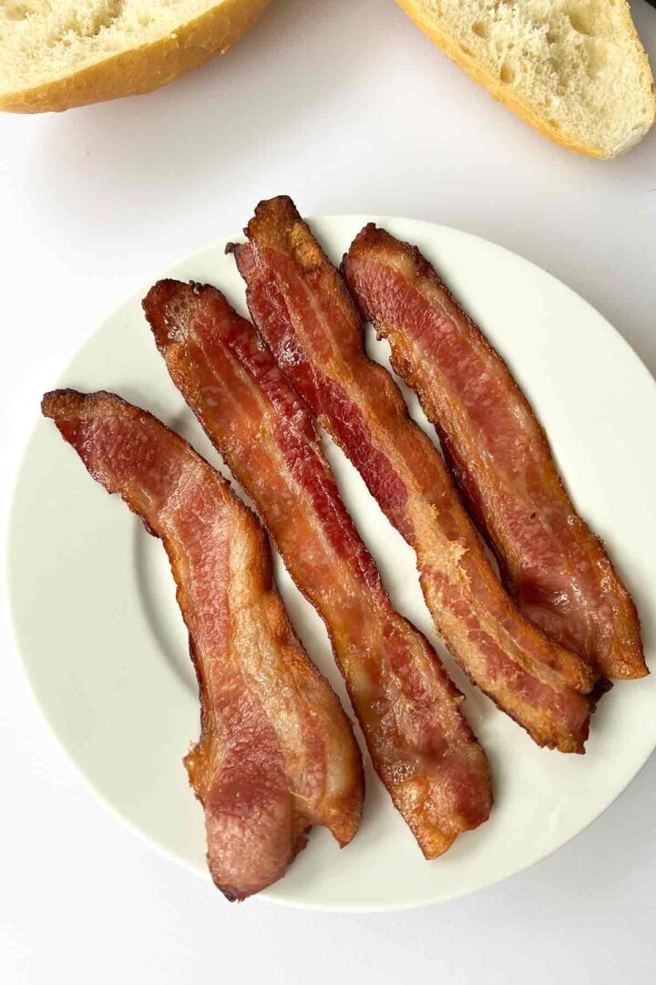 Bacon-cooked-in-the-oven-on-a-plate with bolillo bread above it.
